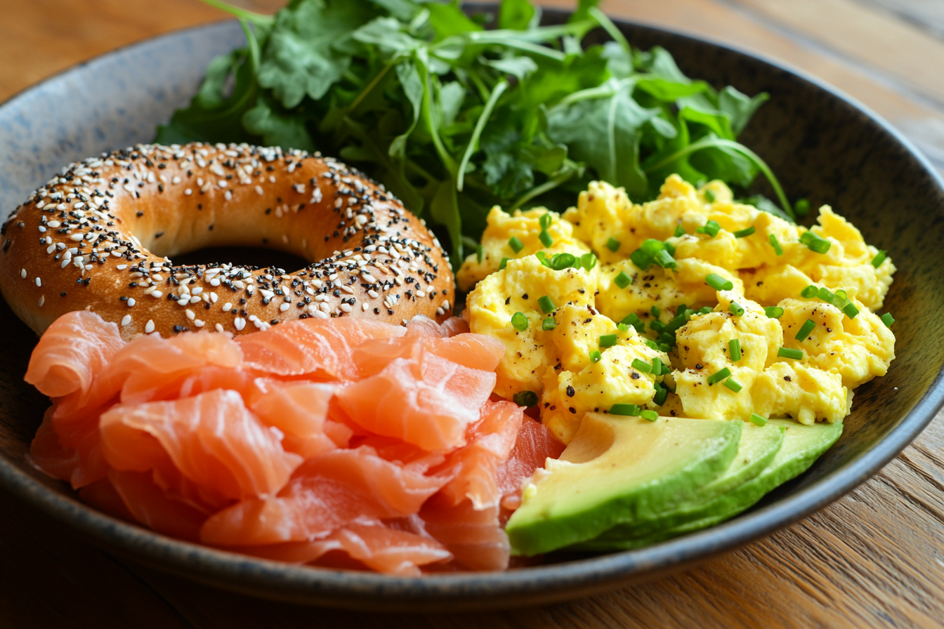 A vibrant breakfast spread featuring smoked salmon bagels, scrambled eggs, avocado slices, and fresh greens.